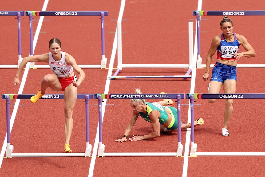 An Australian athlete lies on the track in pain after hitting a hurdle, as competitors race either side of her. 