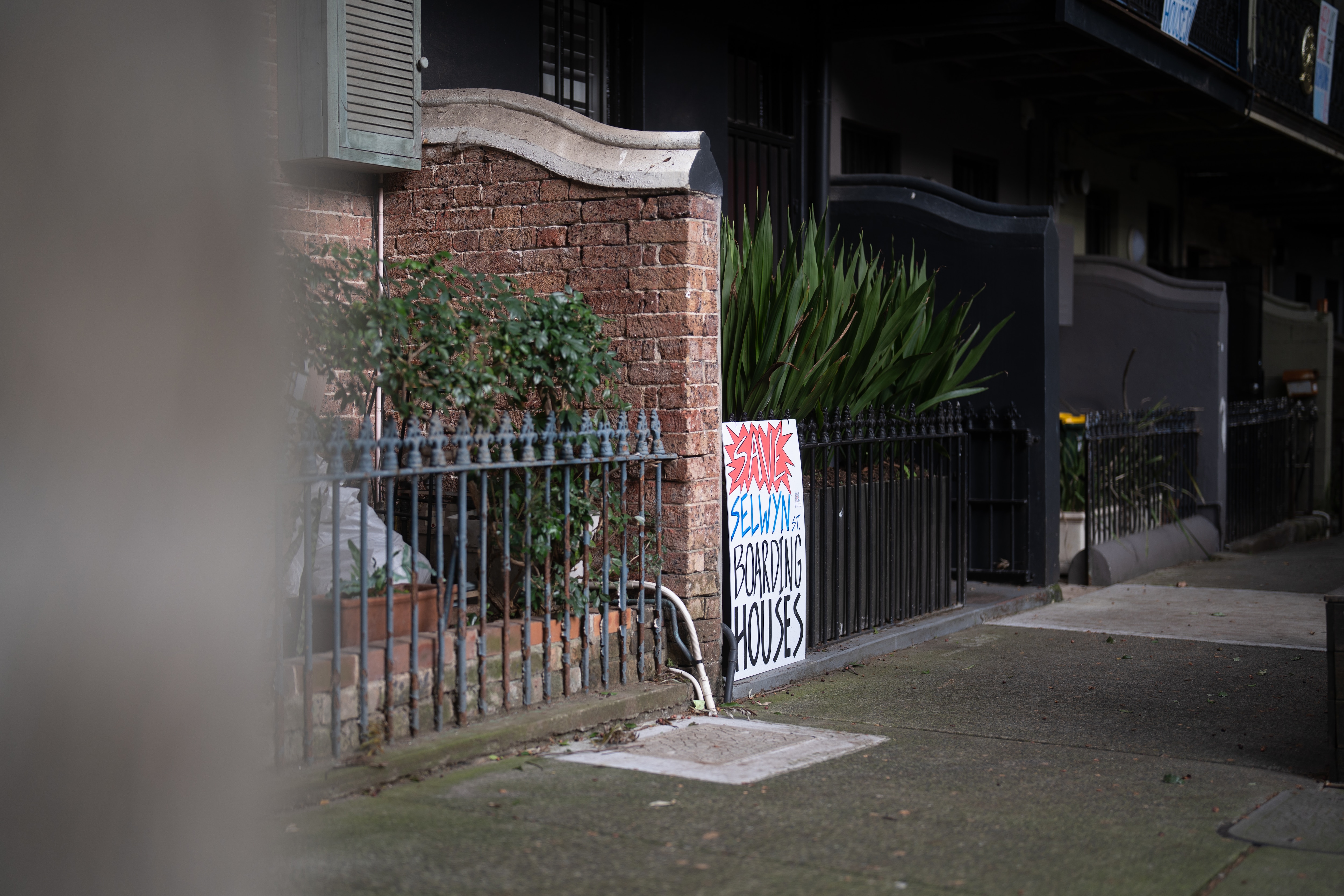 A sign that reads "save our Selwyn st. boarding houses" leaning up against a black painted house
