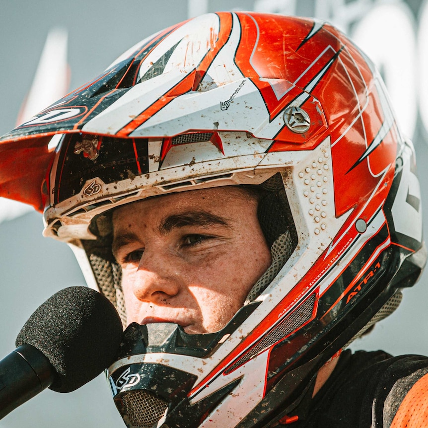 A teenage boy with a motorcross helmet answering a question in to a mic