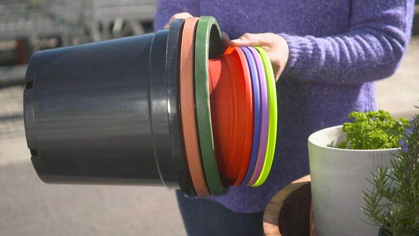 Person holding a stack of coloured plastic plant pots.