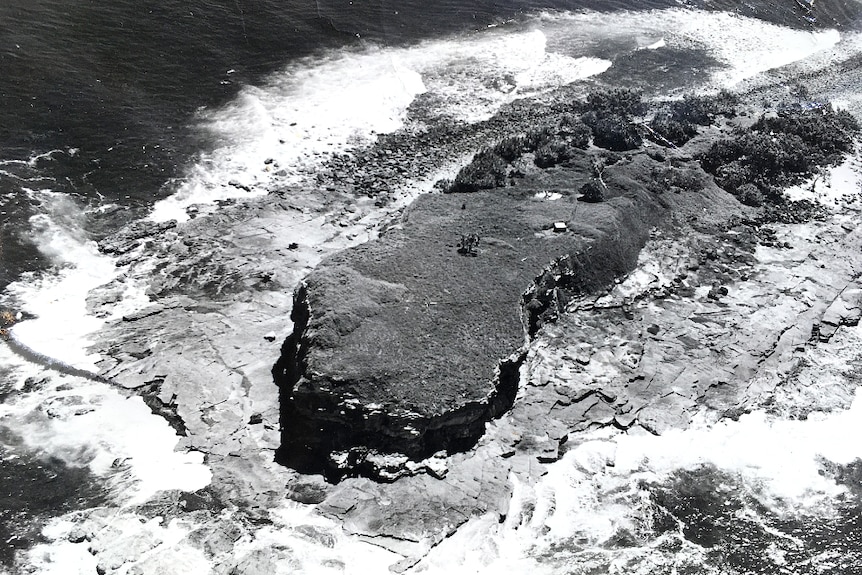 Black and white aerial of a small island showing one structure on the island.