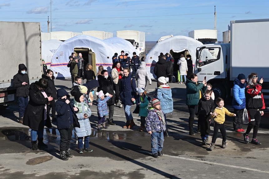 People mill around on tarmac in front of several long arched tents.