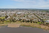 An aerial  photo of a country town built on the edge of a lake, surrounded by green paddocks and hills.