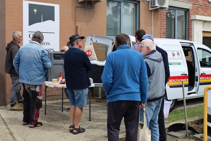 People mill about behind an open van where food is handed out.