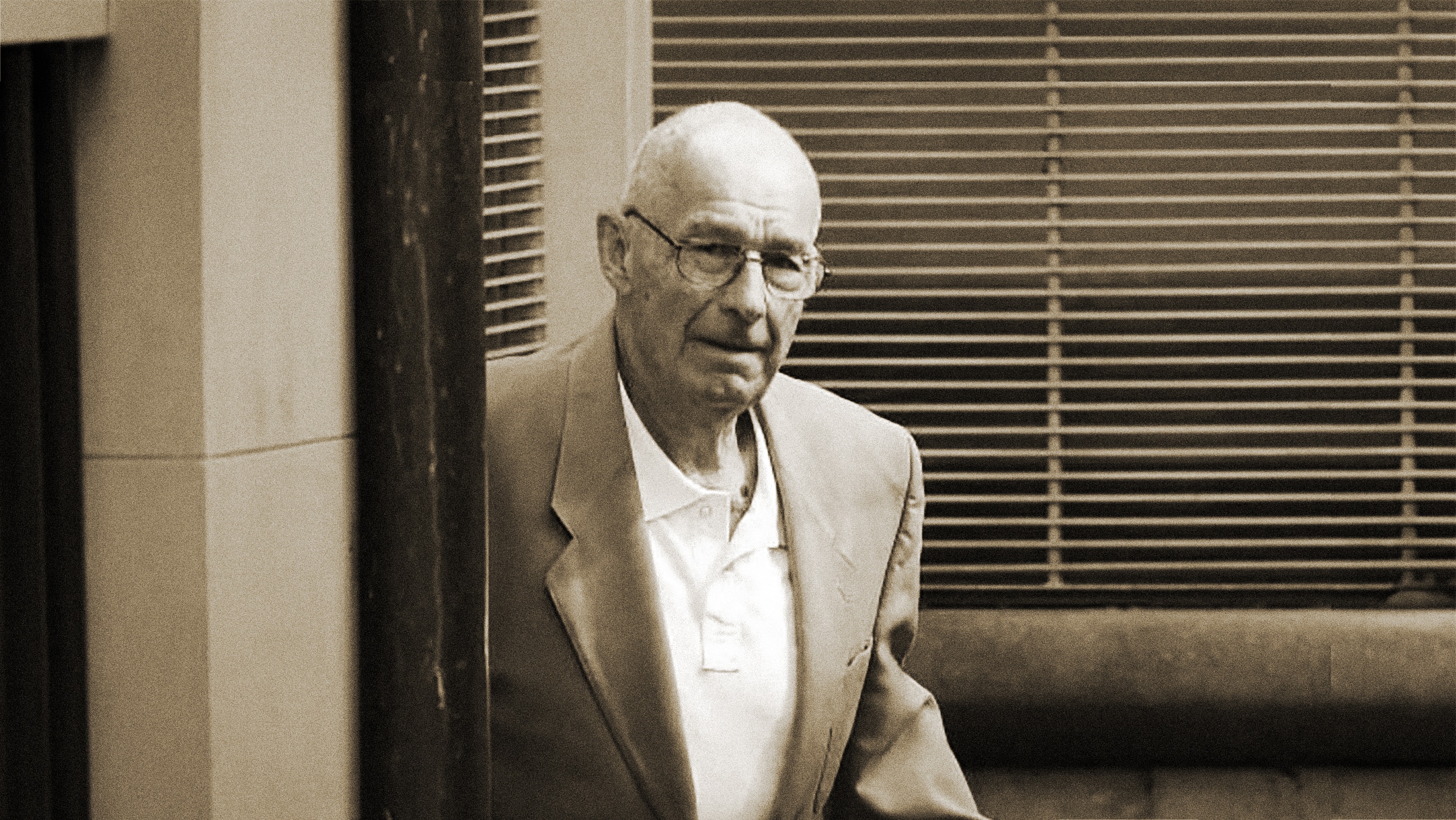 Roger Rogerson, a man wearing glasses, blazer and shirt leaves a building