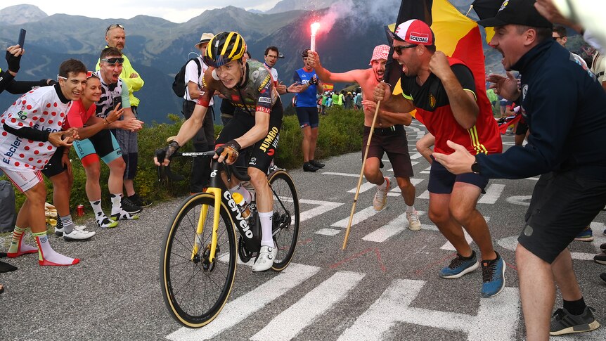 A cyclist grits his teeth as he pedals up a mountain as fans at the roadside cheer, wave banners and flares.