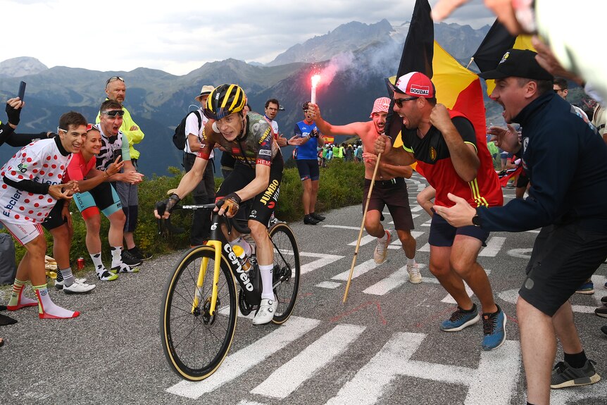 A cyclist grits his teeth as he pedals up a mountain as fans at the roadside cheer, wave banners and flares.