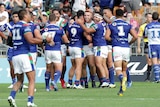 Players crowd around a tryscorer in a rugby league match in Auckland.