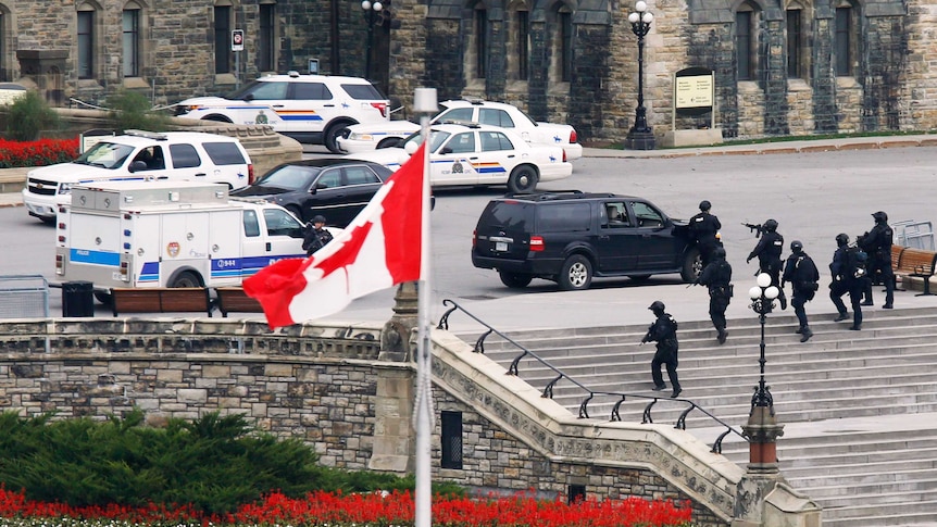 Armed police officers move across Parliament Hill following the shooting in Ottawa.