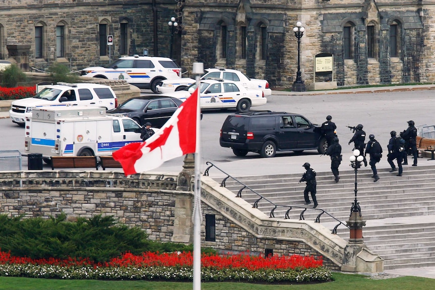 Armed police officers move across Parliament Hill following the shooting in Ottawa.