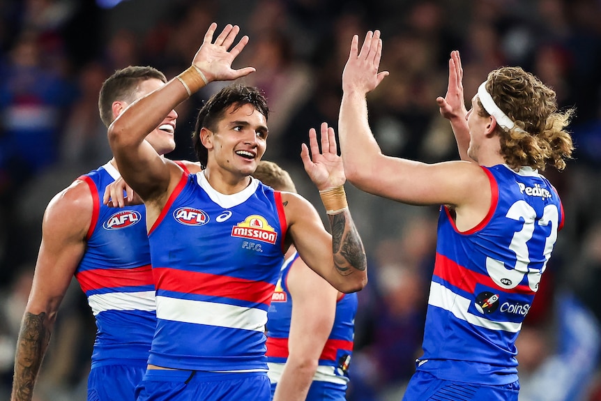 A Western Bulldogs forward smiles at a teammate and raises his hands for a high-five after a goal.