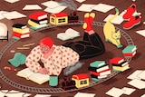 A person lies on their stomach reading a book on the floor, while a model train set bearing more books circles them.