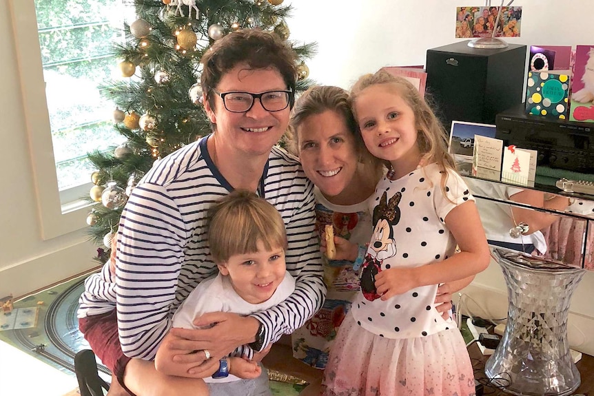 Kiri Stejko with her husband and two kids, with a Christmas tree and cards in the background.