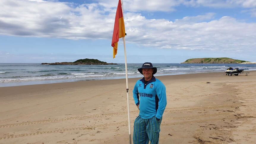 A surf lifesaver stands on a deserted beach near a flag