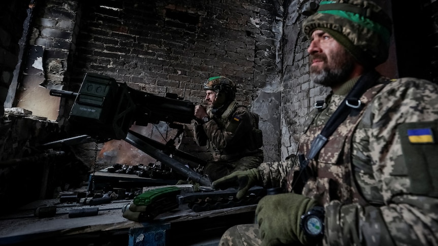 Two soldiers keep watch next to an automatic grenade launcher.