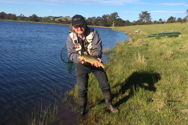 A fisherman besides a river holding a fish.