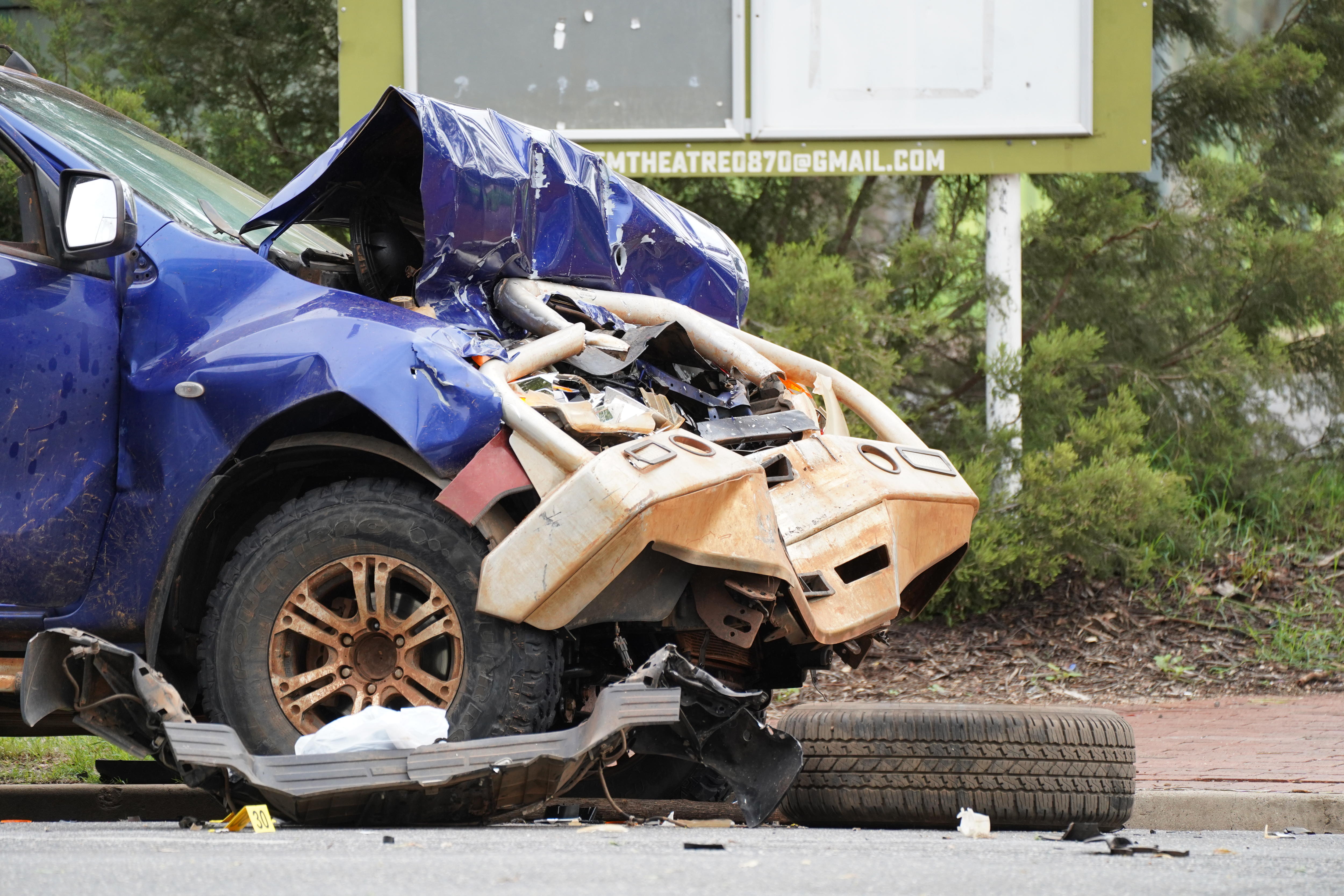 La parte delantera de un tren subterráneo azul está arrugada y hay un neumático tirado en la carretera cercana.
