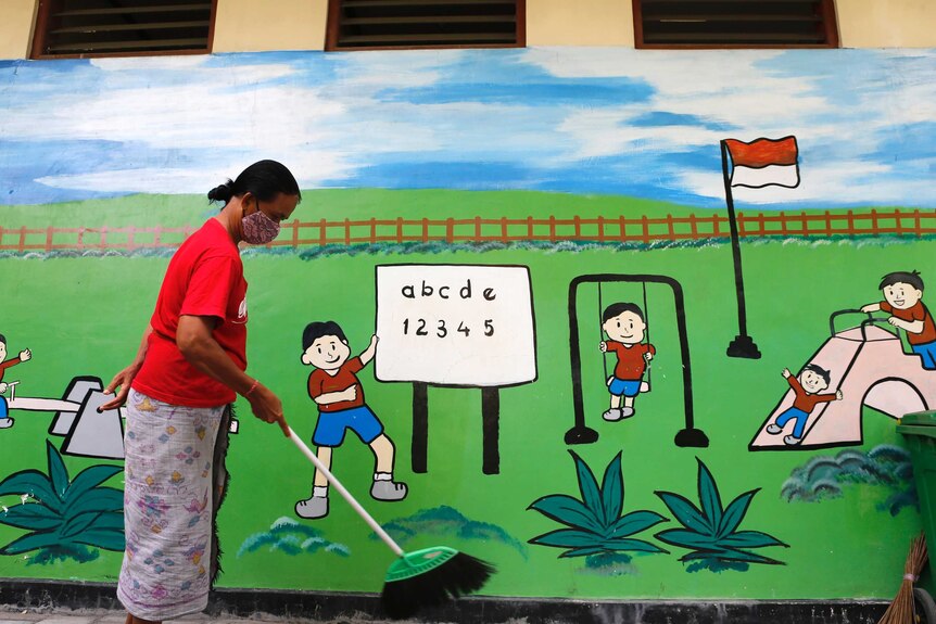 A woman wears a face mask while sweeping an empty school in Bali