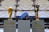 Two football World Cup trophies are seen on pedestals in a stadium, with a half-football on a pedestal between them.