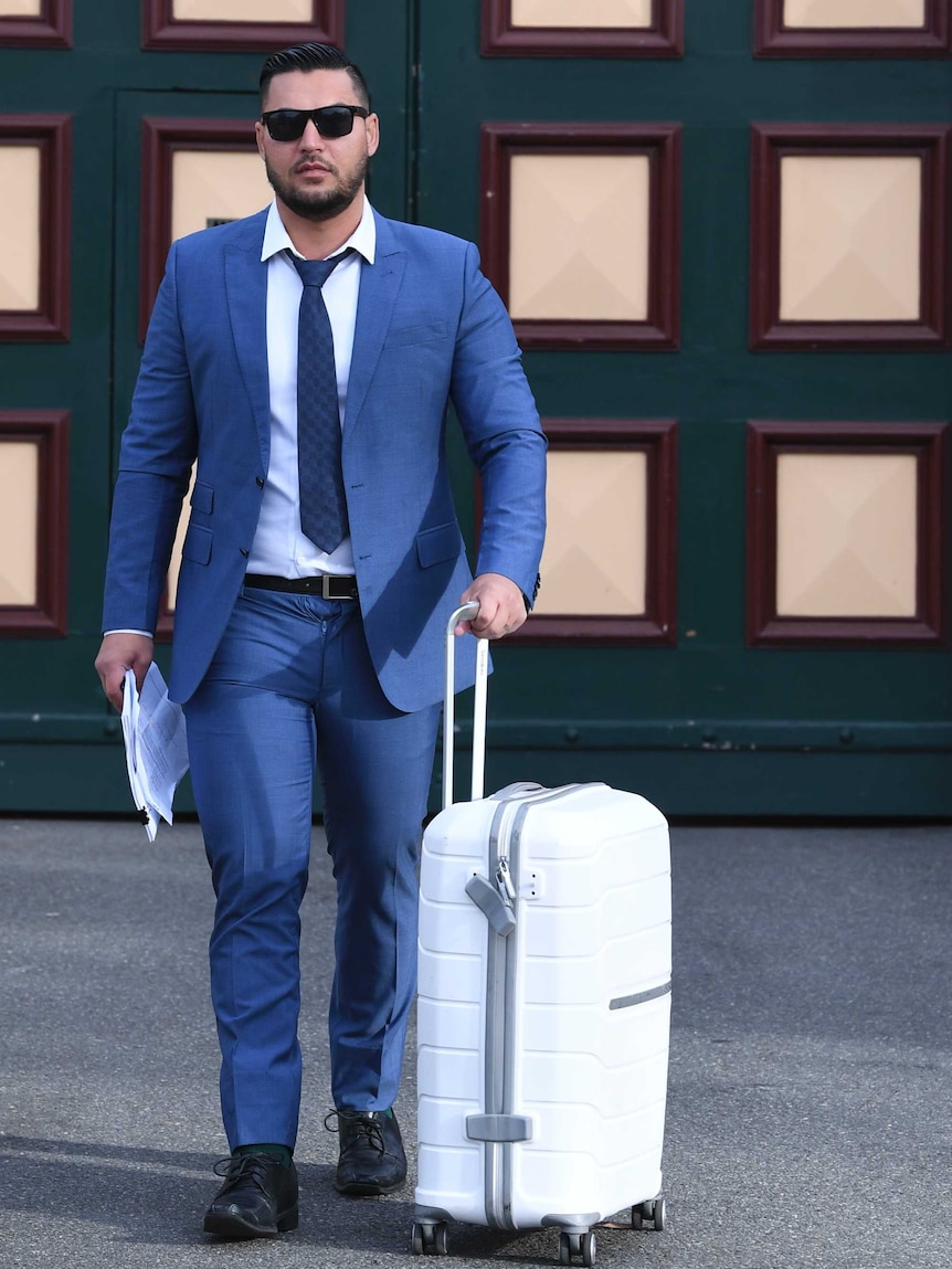 Salim Mehajer wears a suit and wheels a large suitcase as he exits the jail