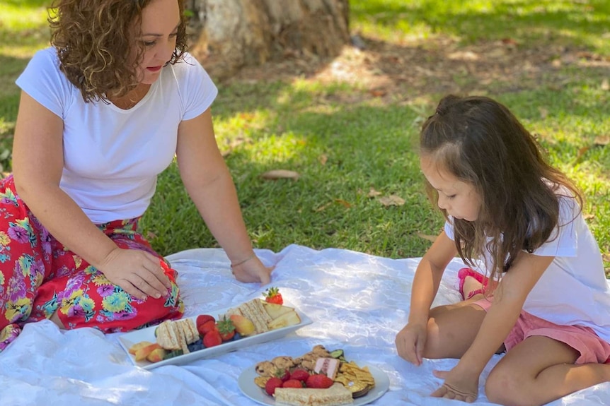 Mum and nutritionist Tara Leong sits on the ground looki at picnic food including sandwiches with six year old daughter