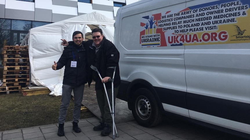 Two men standing in front of a large van and a building