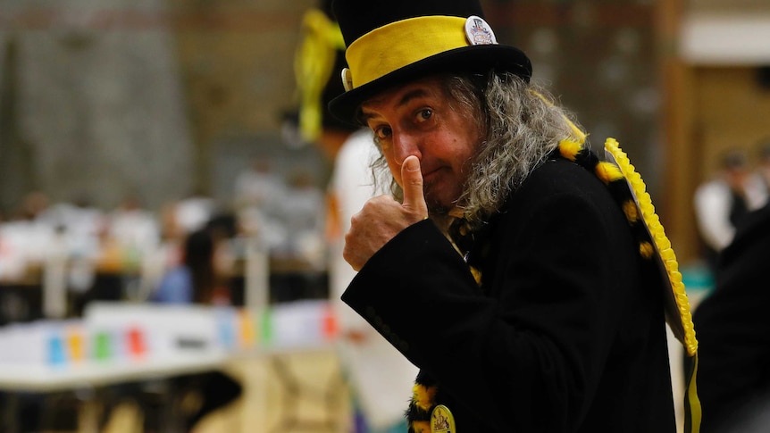 A member of the Monster Raving Loony Party, wearing a top hat, gives the thumbs up to the camera.