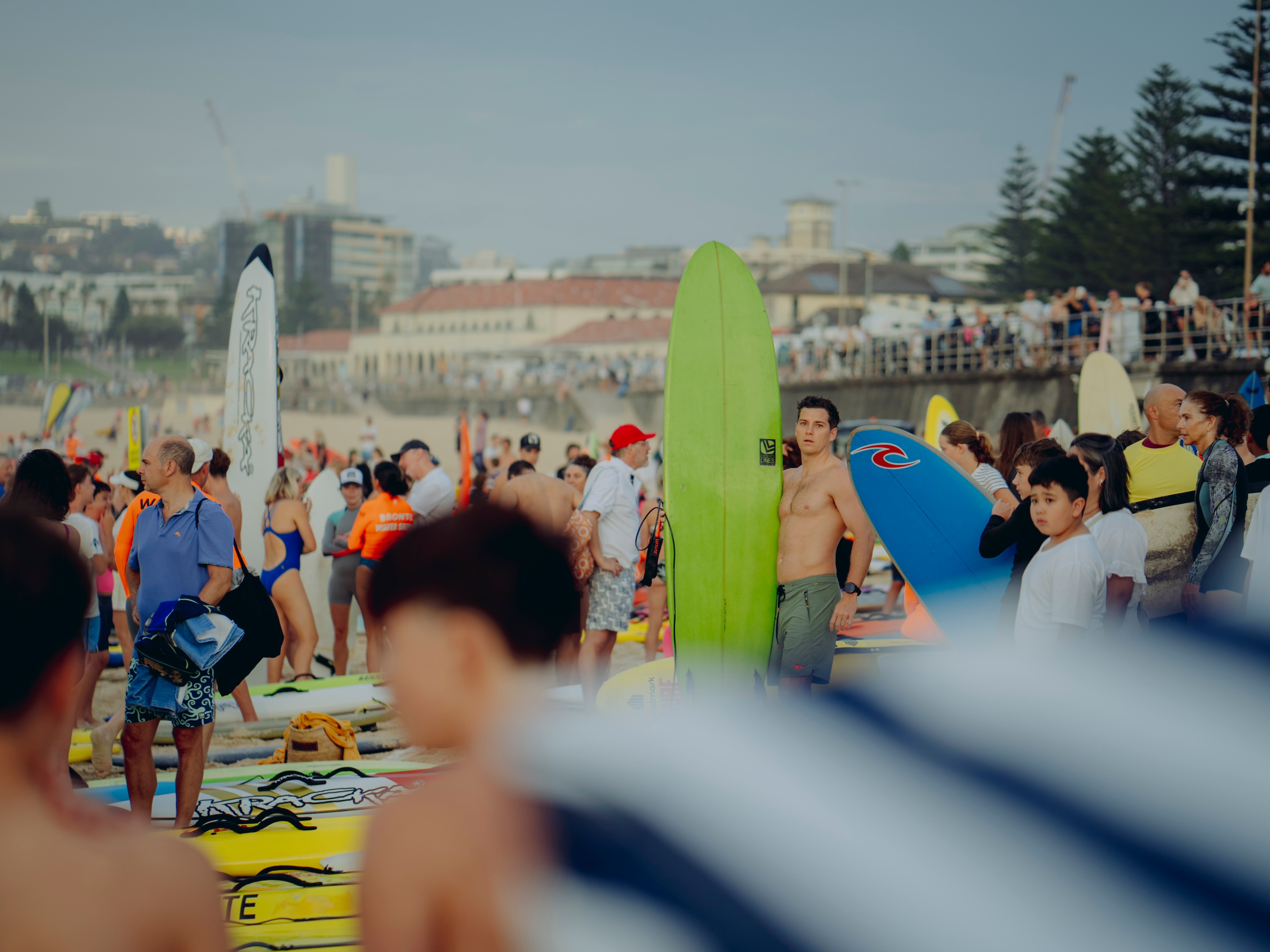 Uma grande multidão de pessoas com paddleboards e pranchas de surf está na areia. 