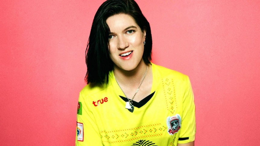 Press image of Romy Madley Croft from The xx; subject in yellow top, against pink background