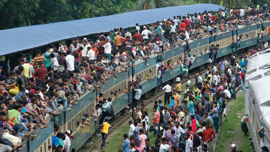 Passengers climb to board an overcrowded train at a railway station in Dhaka