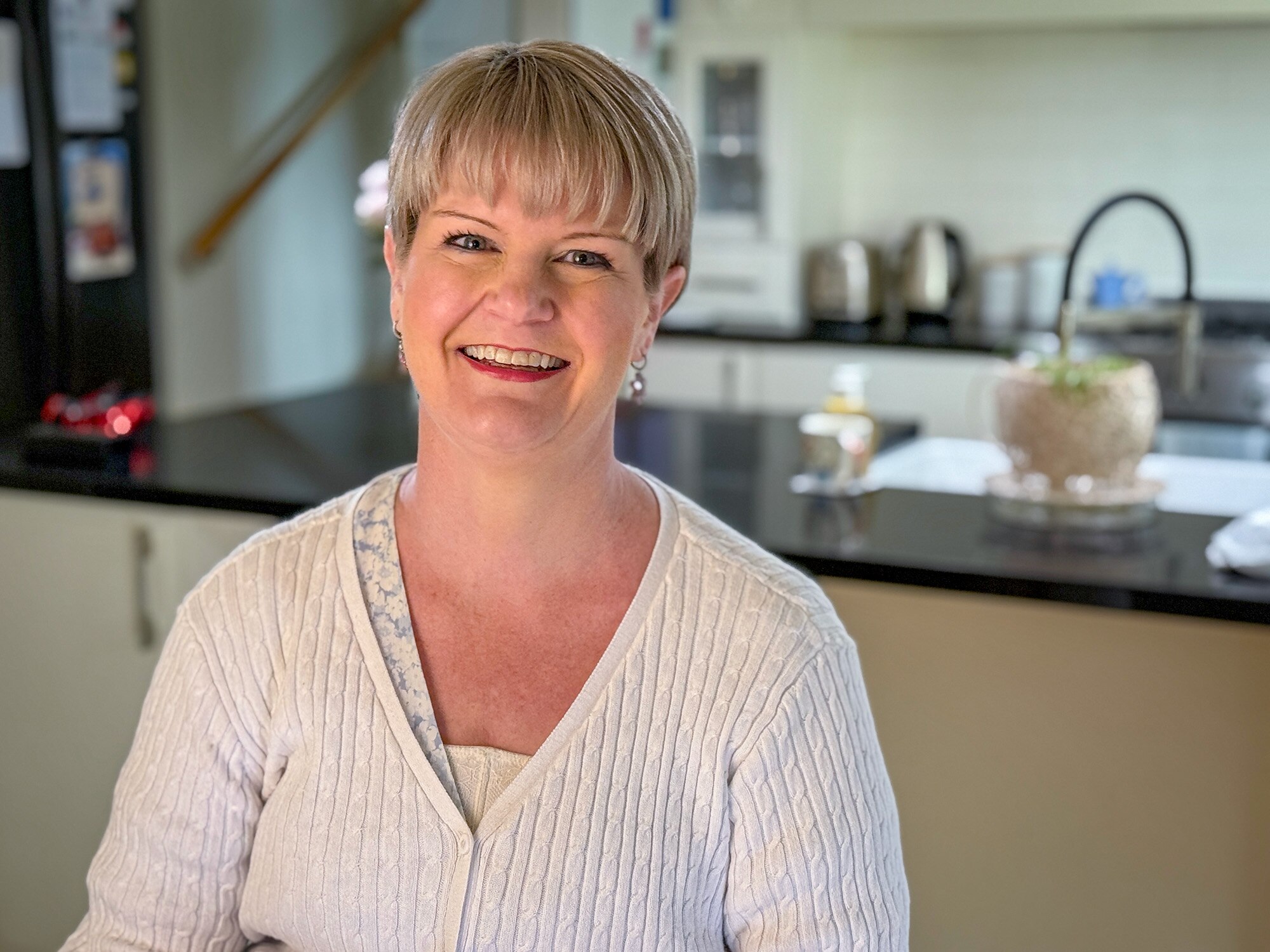 Una mujer caucásica con flequillo rubio sonríe en una cocina