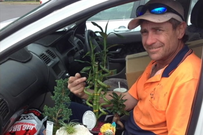 A man sits in the passenger seat of a car holding a bunch of plants.