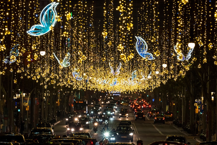 yellow and blue christmas lights hang above an avenue in Barcelona, Spain with cars driving below