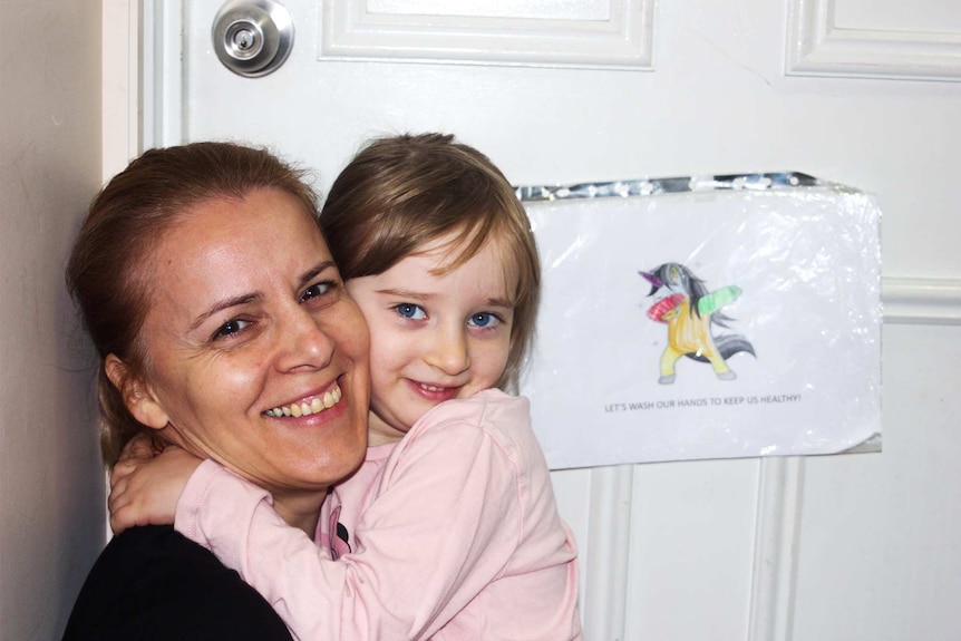 Dr Zerina Tomkins and Emma hug in front of a sign on their door with a reminder to wash their hands.