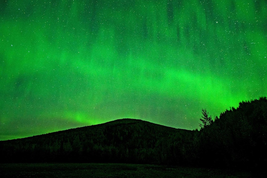 Stunning green light in night sky over mountains.