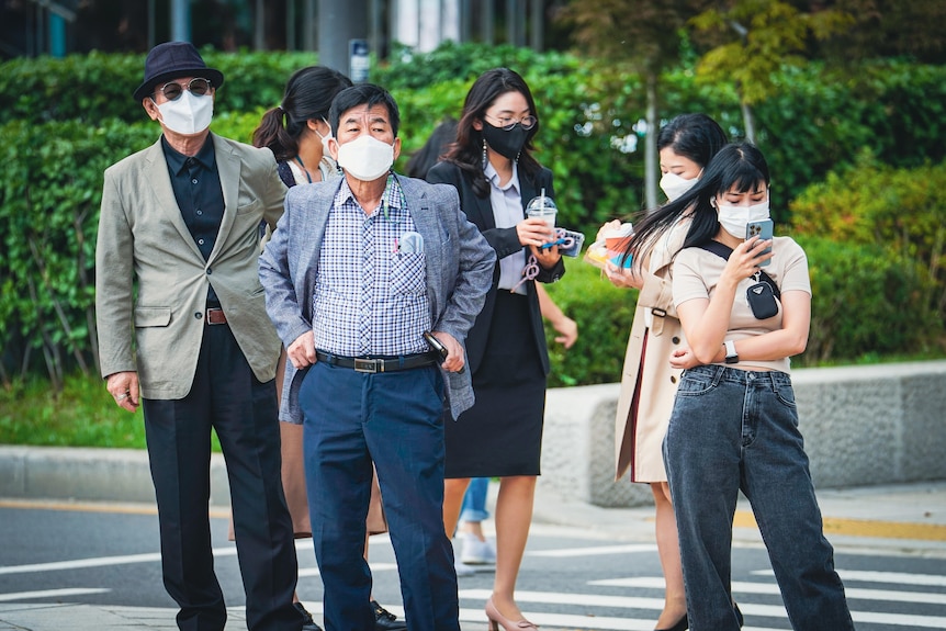 A group of Koreans, all in face masks, standing at a street corner