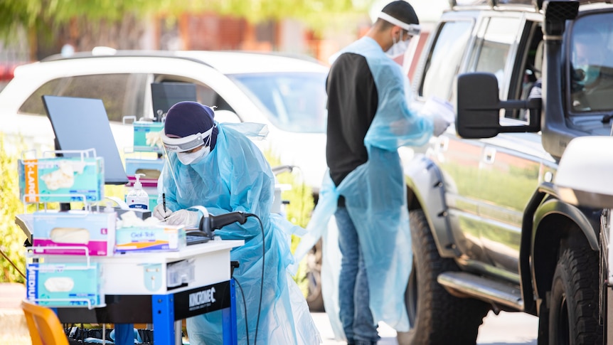 Two people in PPE, one near a car, another working on a trolley.