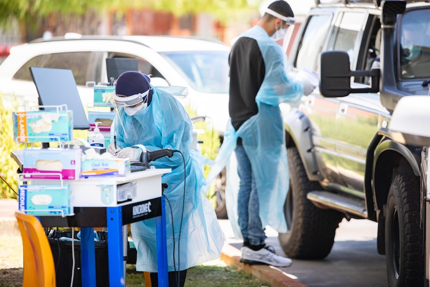 Two people in PPE, one near a car, another working on a trolley.