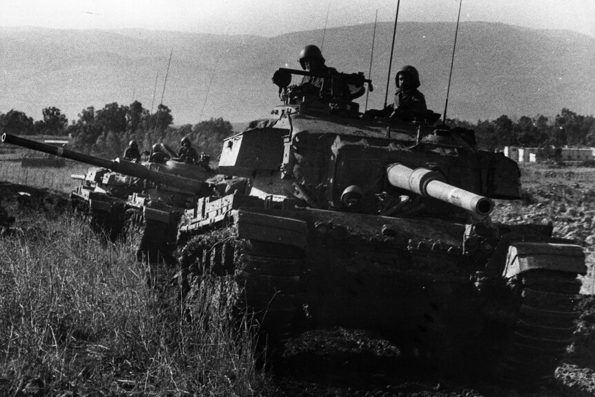 A black and white photo from the 1970s of a line of tanks in grass