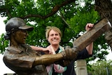Australian cricket great Belinda Clark smiles as she stands behind a bronze statue of her playing an attacking shot.