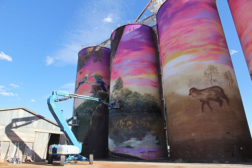 Two artists on a lift paint a 30m silo wall.
