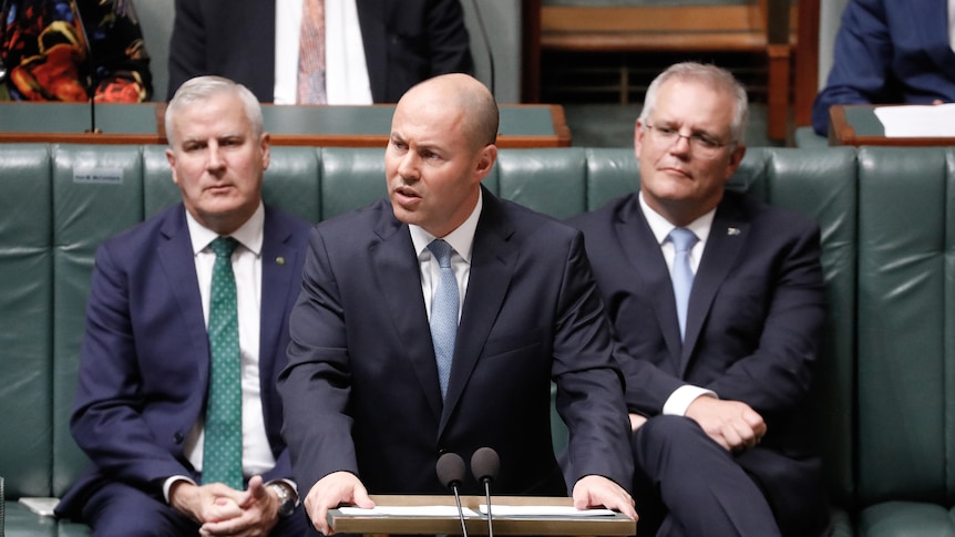 Josh Frydenberg, wearing a dark blue suit and light blue tie, stands at a lectern.