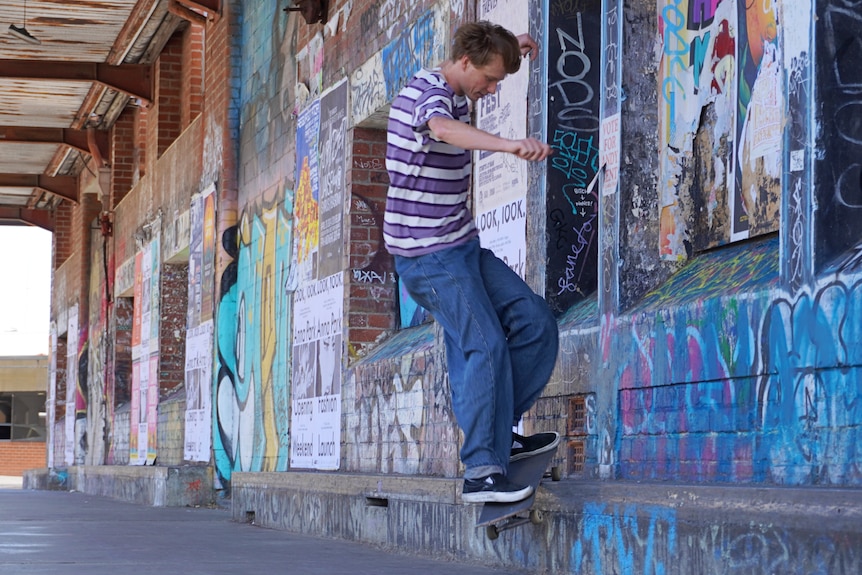 Rowan White in a striped shirt and jeans, riding a skateboard at Fremantle's Woolstores.