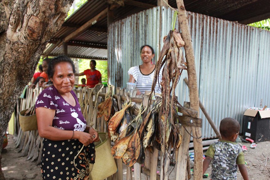Two women with fish and octopus drying on a fence near a tin shed on Atauro Island, East Timor
