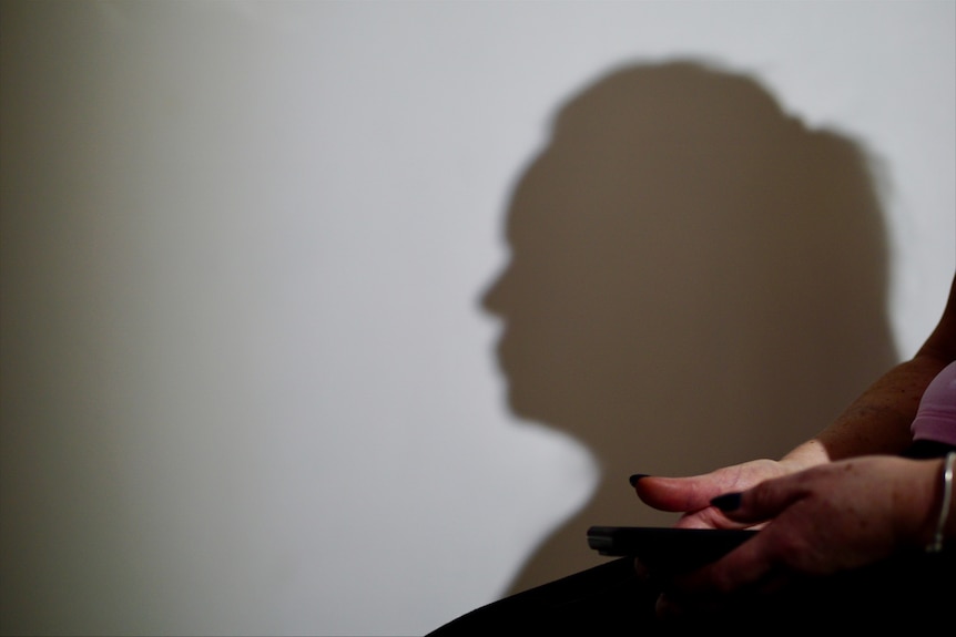 The shadow of a woman's side profile is projected onto a white wall. Her hands are in the foreground