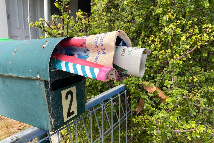 A green letterbox stuffed with junk mail.