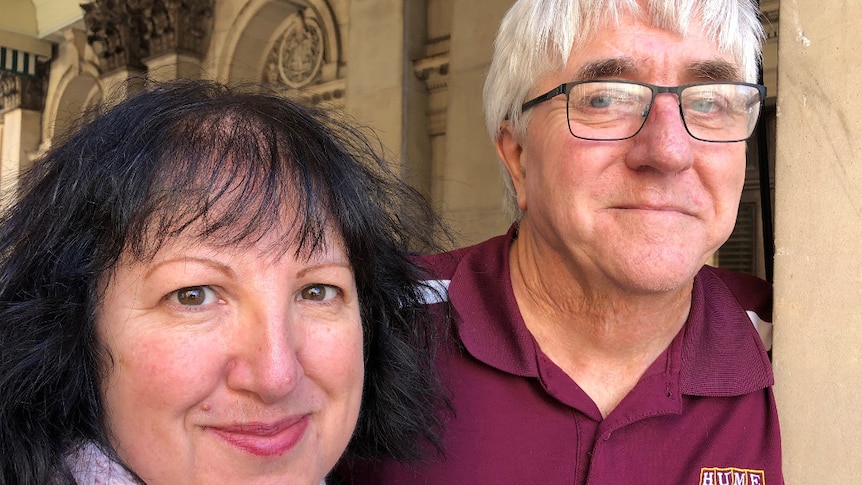 A man with grey hair and glasses stands beside a woman with shoulder-length black hair.