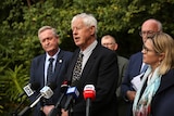 People in suits speak to the media at a press conference