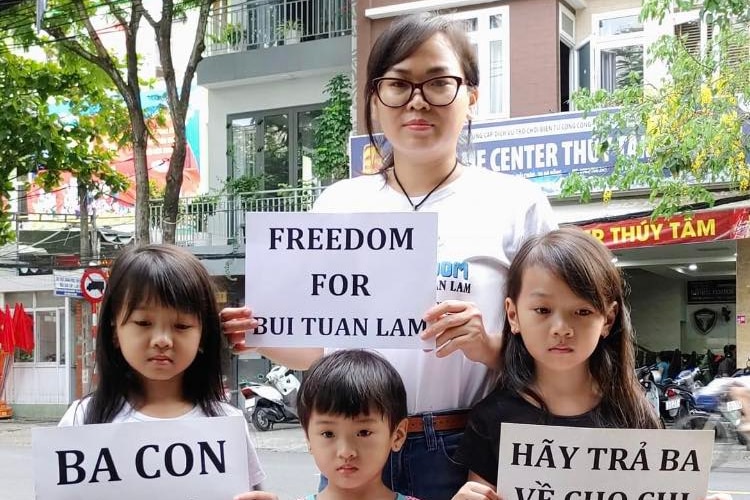 A Vietnamese woman holds a sign saying FFreedom for Bui Tuan Lam" next to three children on a street. 