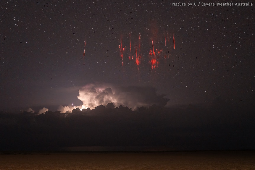 Burst of red light in night sky with thunderstorm in the background